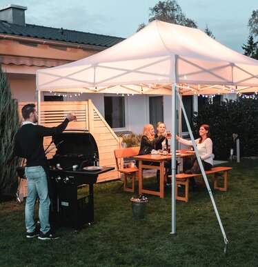 Friends celebrate a barbecue and garden party under the garden tent. The garden tent is festively decorated with fairy lights.