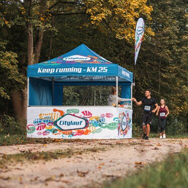 Blue 3x3m event gazebo with custom Citylauf print, with custom flag, closed side wall and half-height side wall with counter used as a refreshment stand at a city race