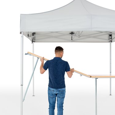 The man assembles the wooden counter on the folding gazebo.